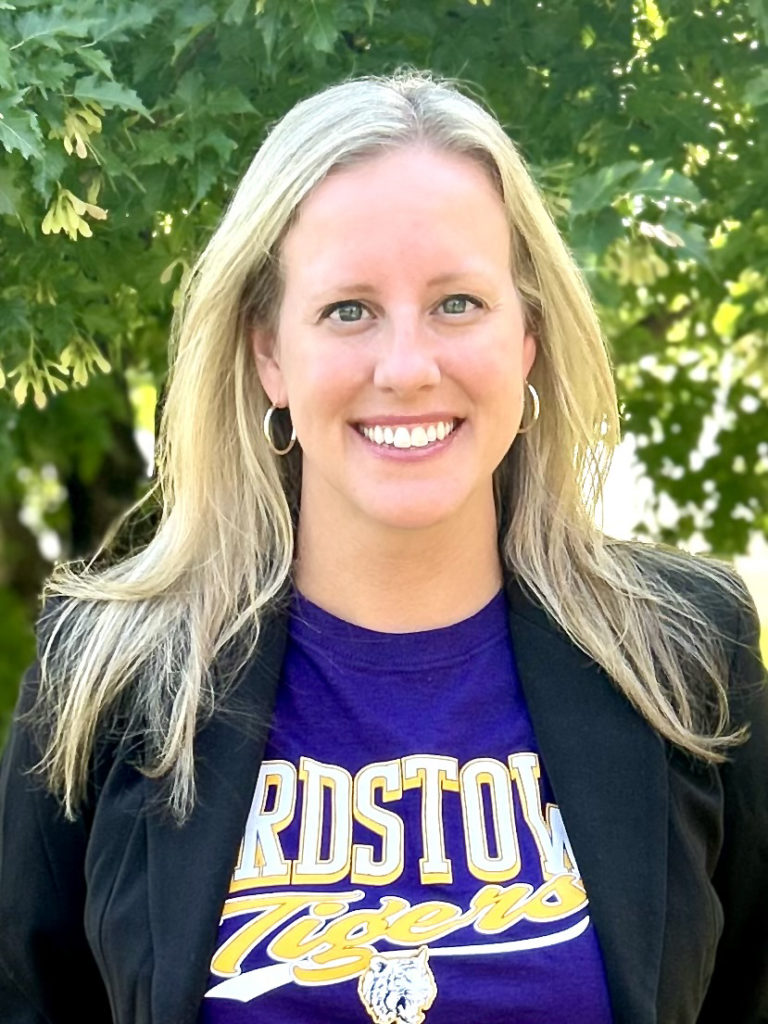 Photograph of Robin McCoy the new assistant principal for Bardstown High School. Robin is wearing a Bardstown tigers shirt and standing in front of a tree.